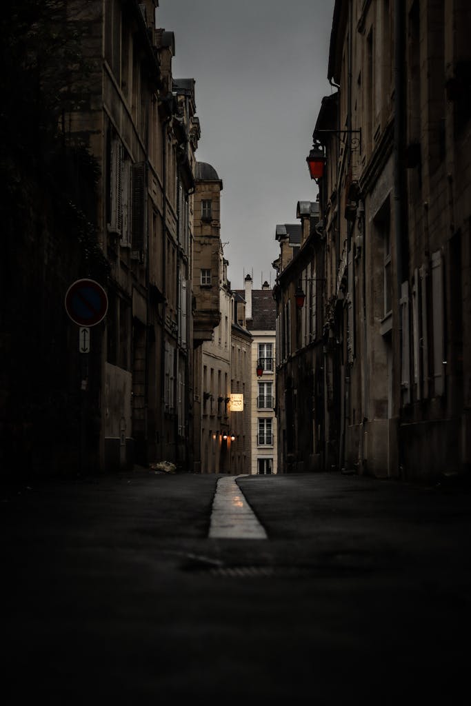 A narrow, dimly-lit alley in Caen, France, showcasing historical architecture under an eerie evening sky.