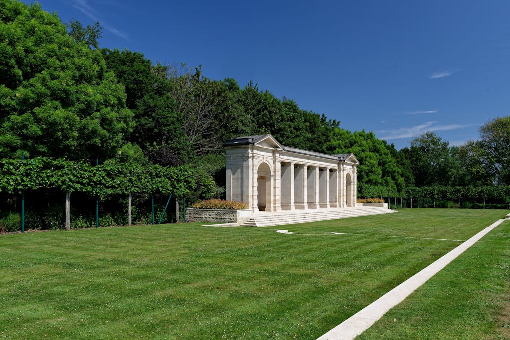 A tranquil landscape of the Bayeux War Cemetery Memorial surrounded by lush greenery in Normandie, France.