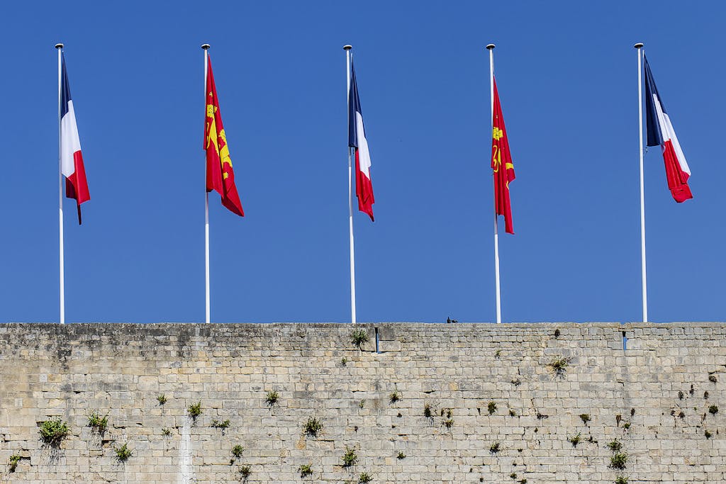 French and Normandy flags on poles above ancient wall in Caen, Normandy, France.