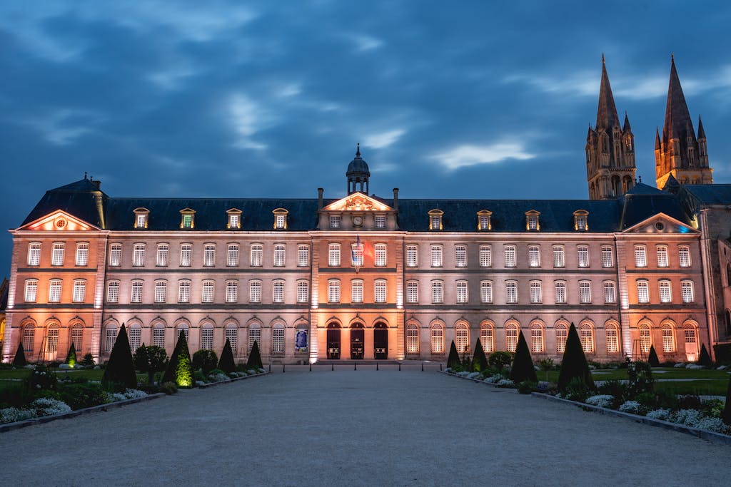 Illuminated facade of a historic abbey at dusk in Caen, Normandy, France. A landmark sight for travelers.