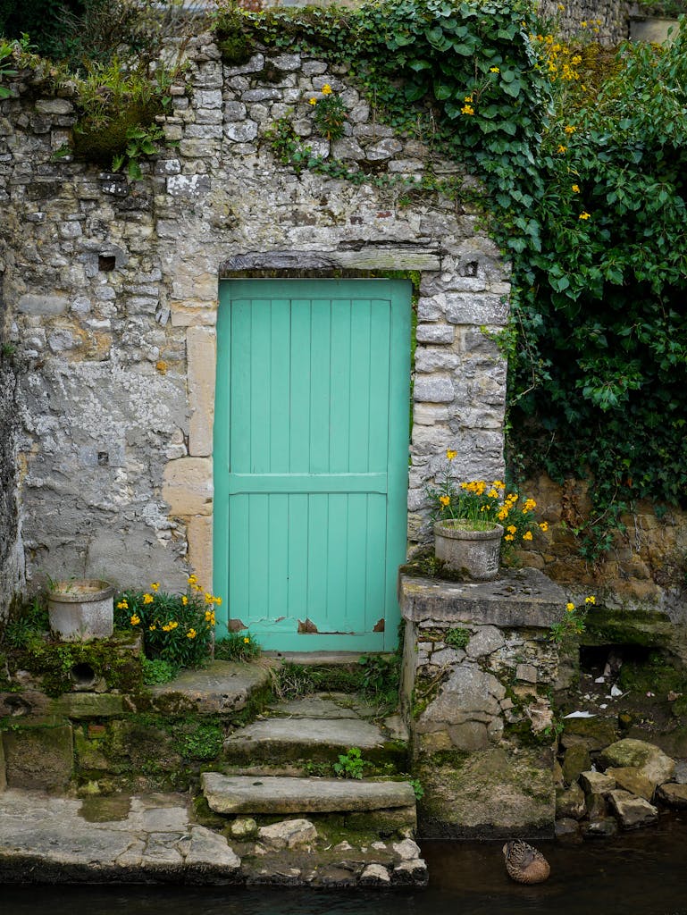 Rustic stone entrance in Bayeux, Normandie with ivy and a turquoise door.