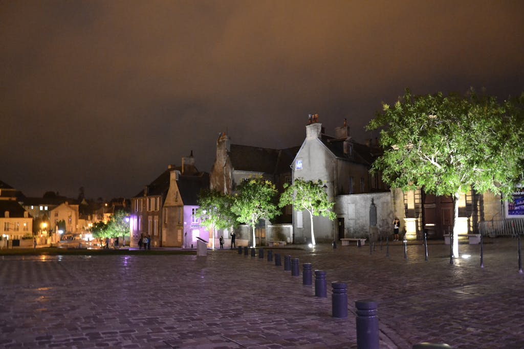 Scenic nighttime view of a historic town square in Bayeux, France, with illuminated trees and buildings.