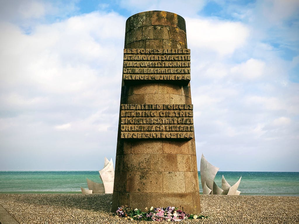 Stone monument honoring Allied forces at Normandy Beach on a clear day.