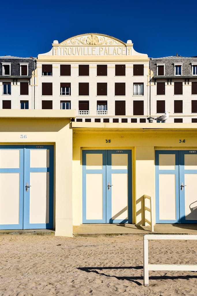 Charming view of colorful beach cabins and historic Trouville Palace in sunlight.