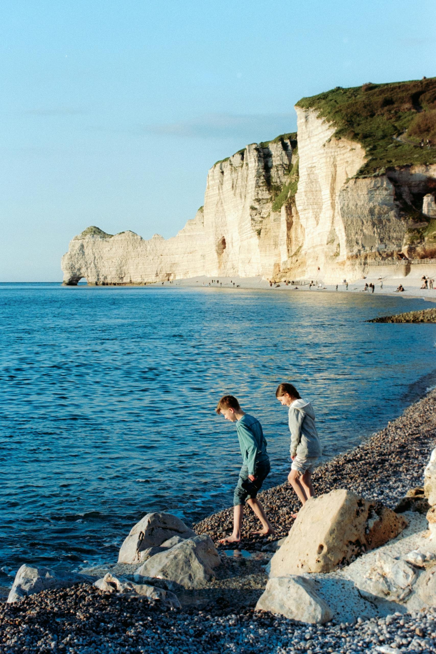 Kids walking along the scenic pebble beach at Etretat Cliffs, Normandy, France.